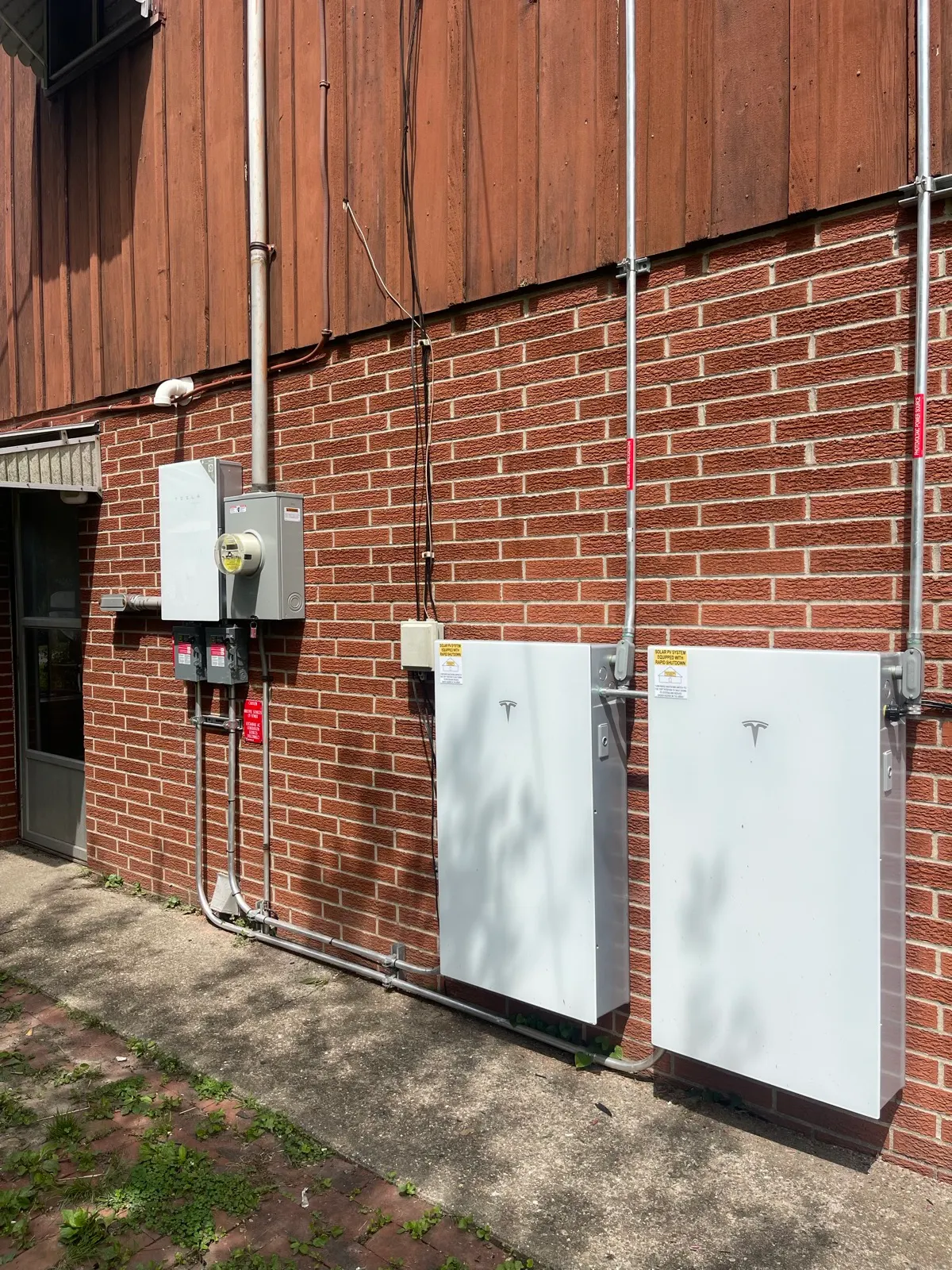 Two Tesla Powerwall home batteries with conduit and a utility meter on a brick exterior wall