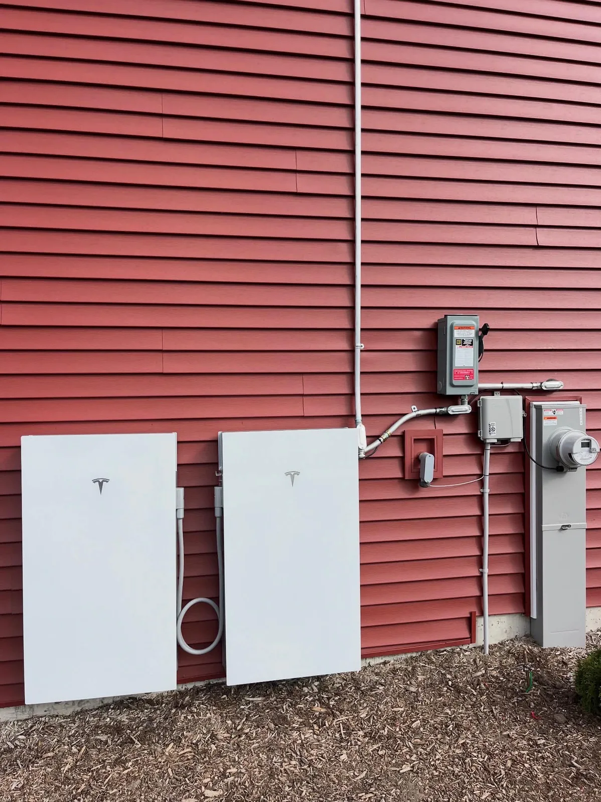 Utility meter, AC disconnect, and two Tesla Powerwall batteries on red siding