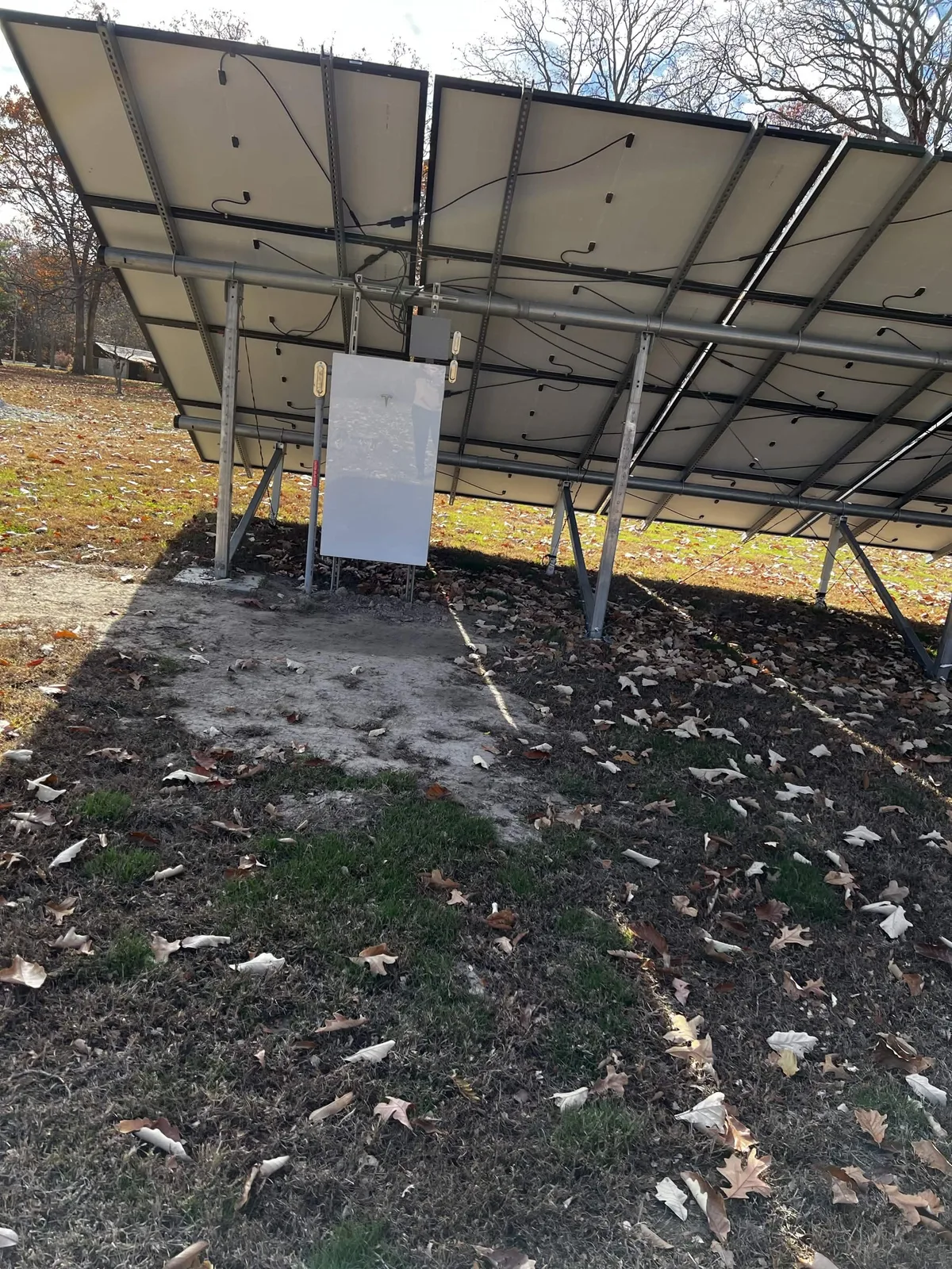 Underside of a ground-mounted solar array showing the steel racking, panel wiring, and disconnect box on an Illinois installation