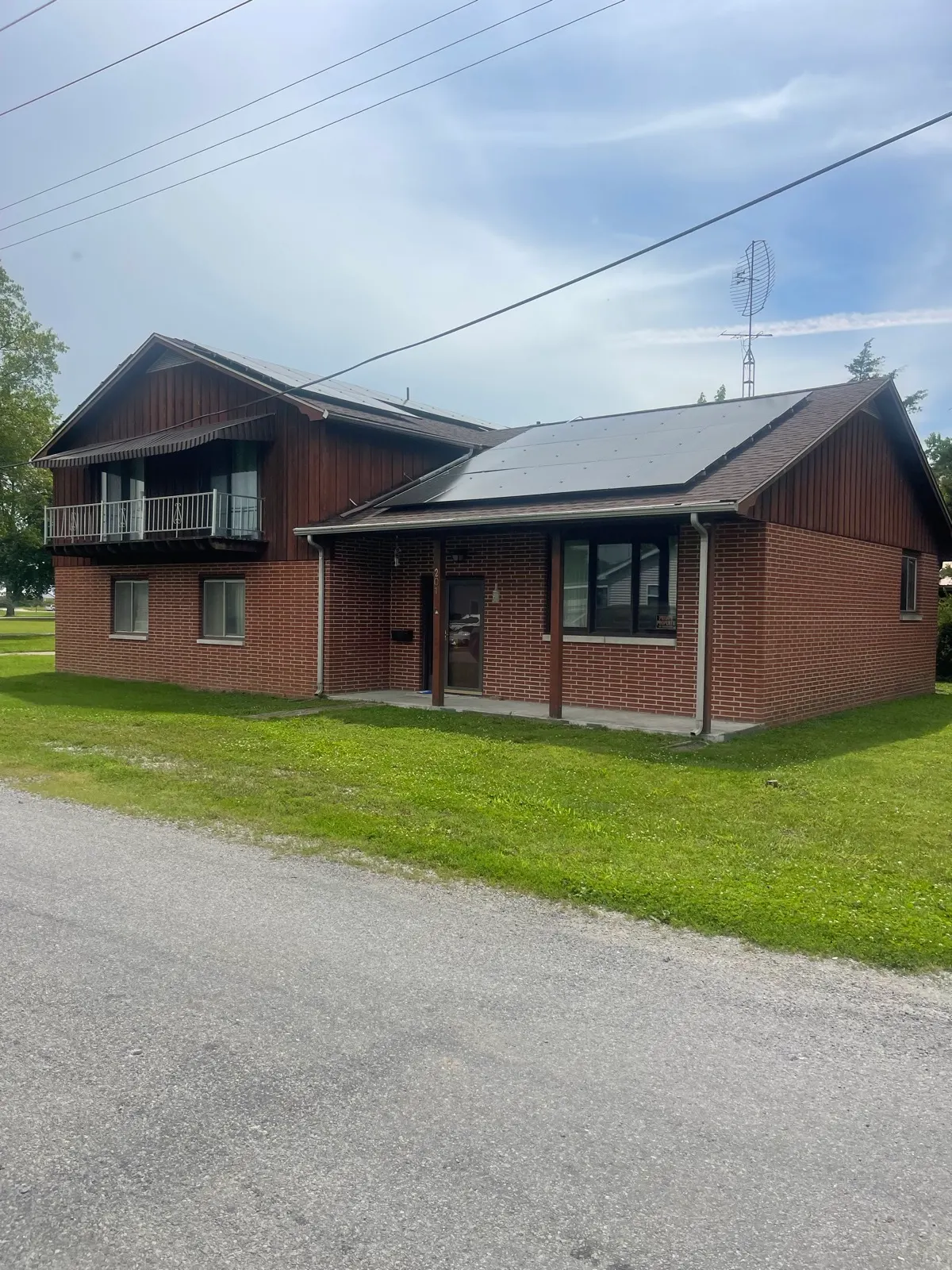Rooftop solar panels on a two-story brick and wood-sided Illinois home along a country road