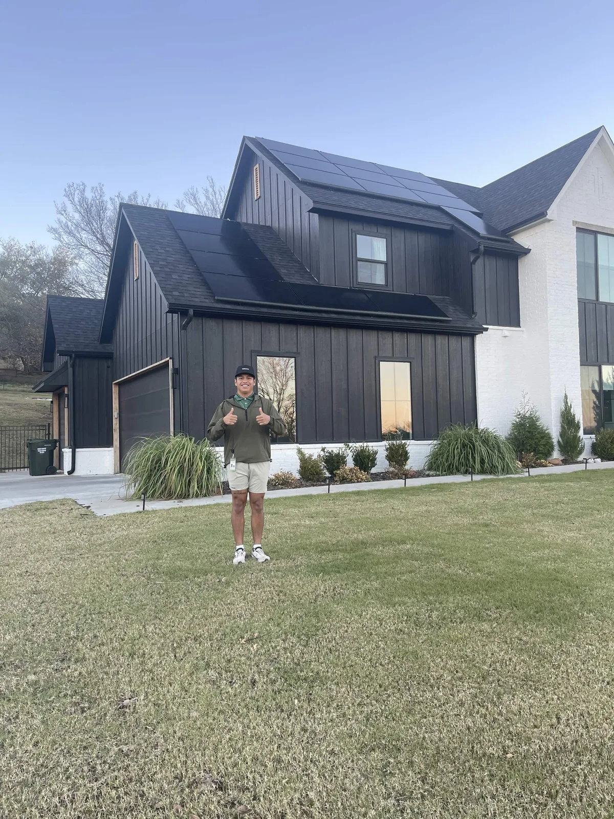Homeowner giving a thumbs up in front of a modern black two-story home with solar on every roof plane