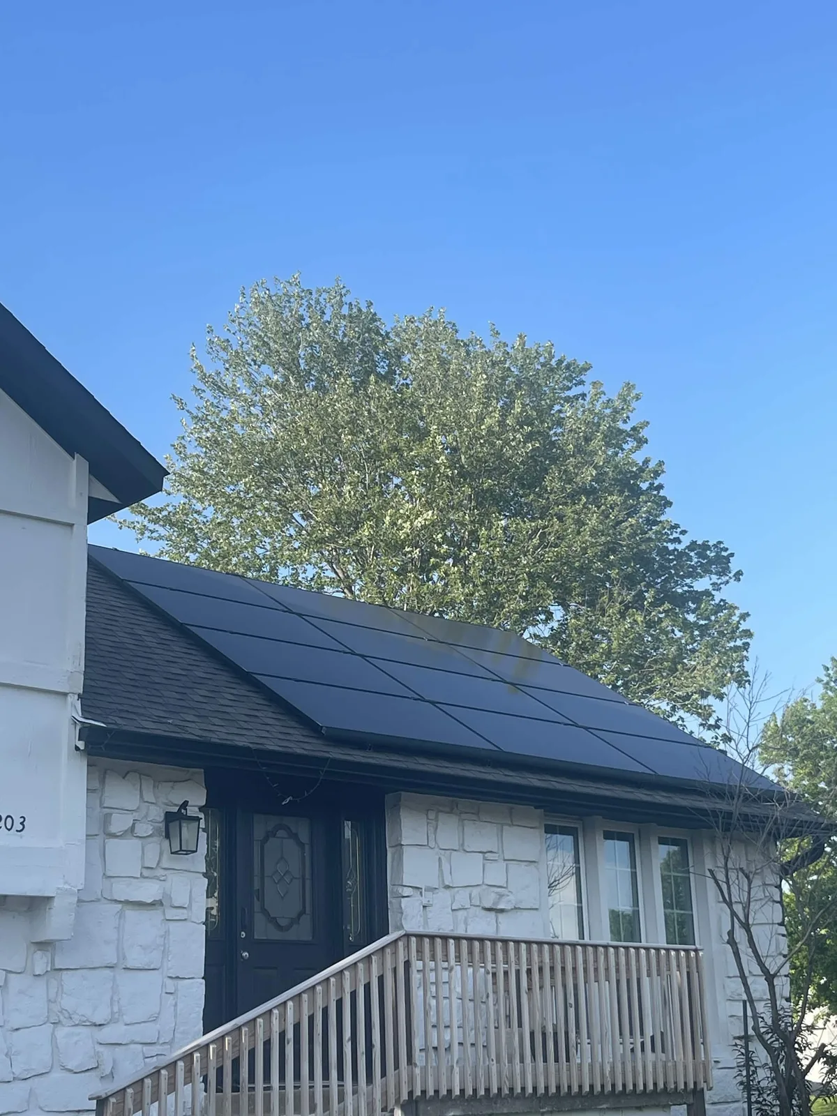 Black solar panels on the roof of a white stone Illinois home with a wooden front deck