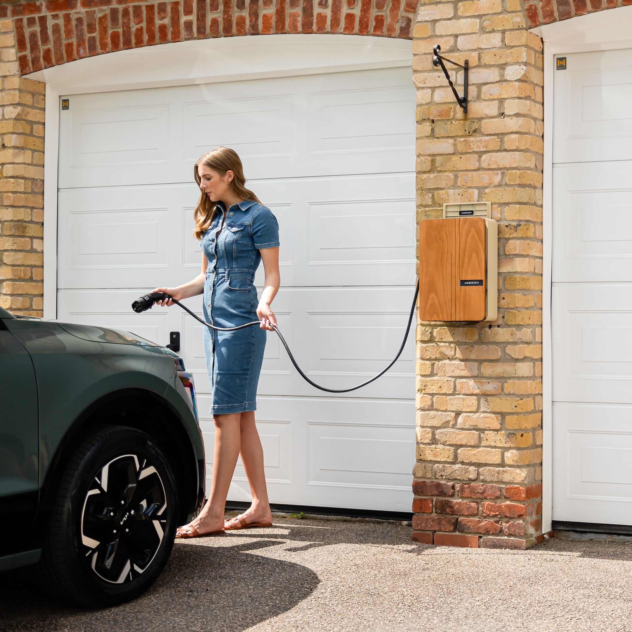 Woman plugging a home EV charger into a green electric vehicle outside a brick garage